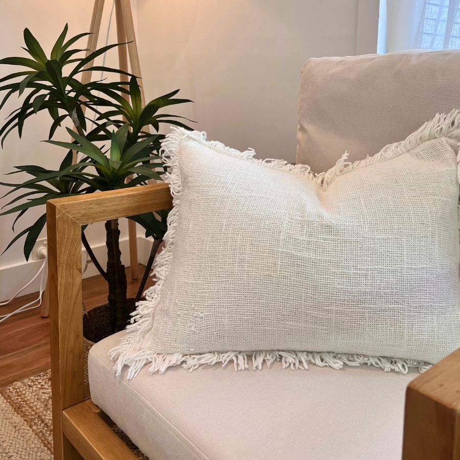 White cushion on a chair with lamp and plant decor.
