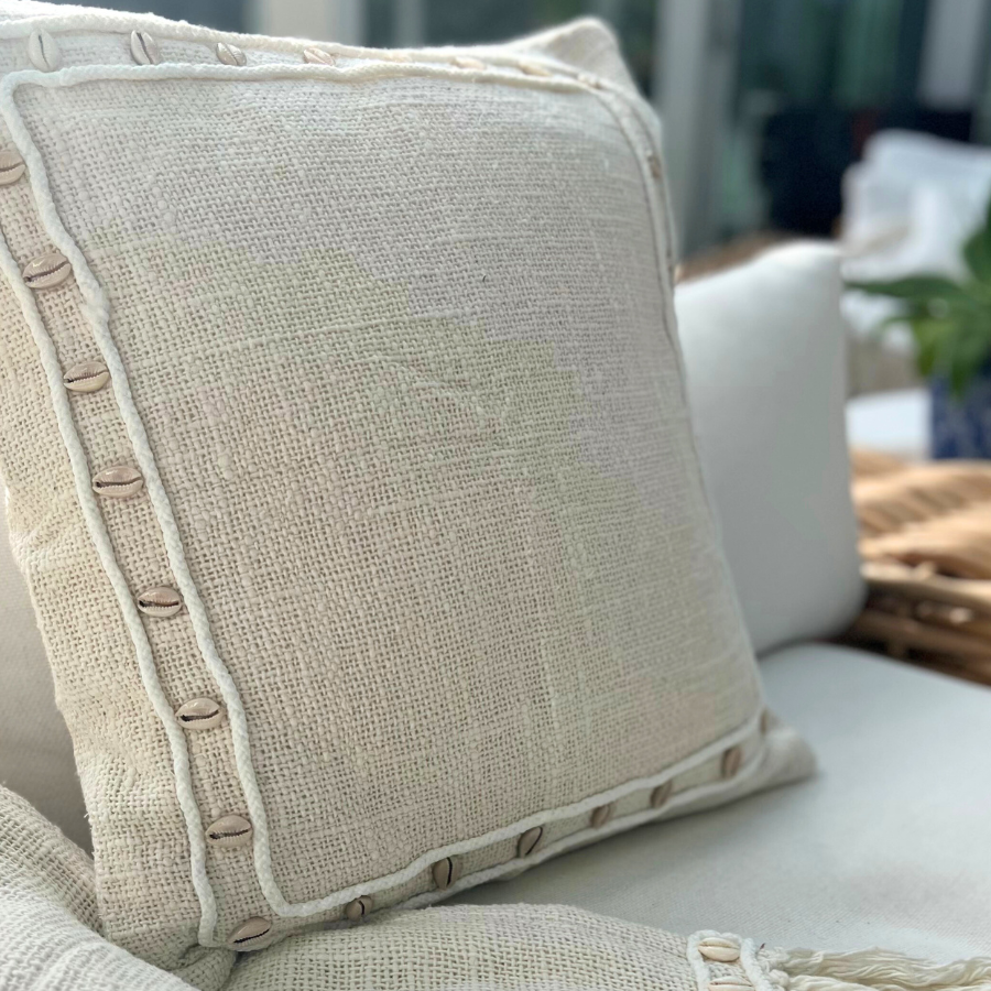 Cushion with shell decor on a sofa with blanket. 