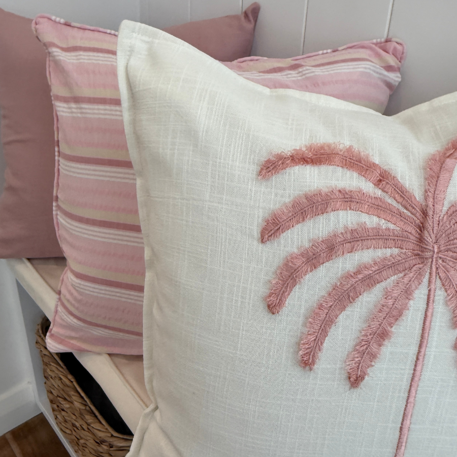 Decorative cushion with palm tree design on a bench with other cushion.