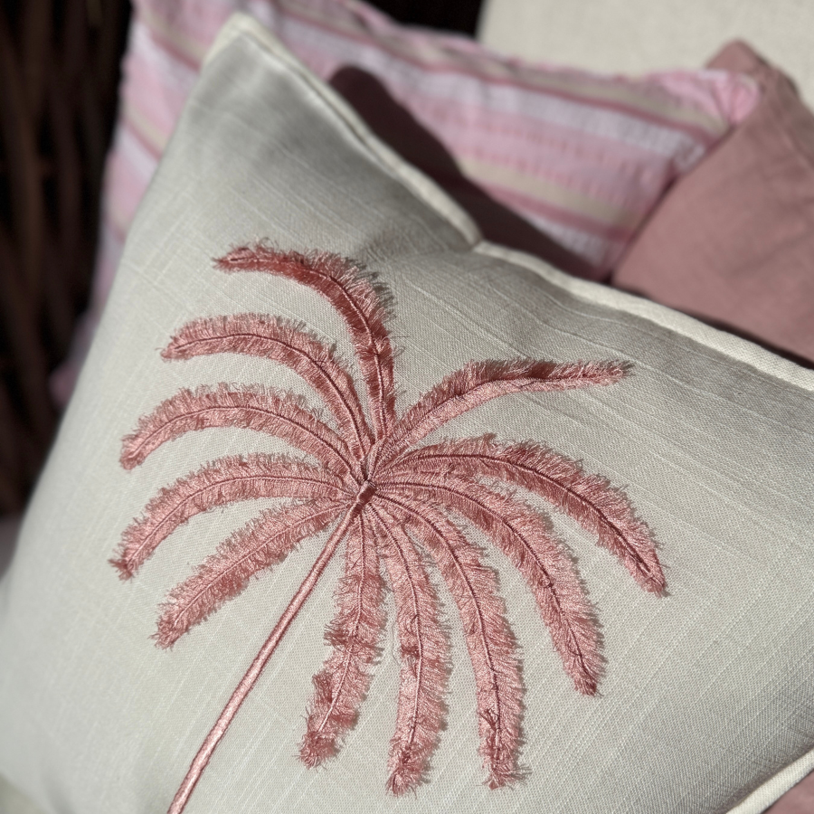 Decorative cushion with embroidered palm tree design on a neutral background.