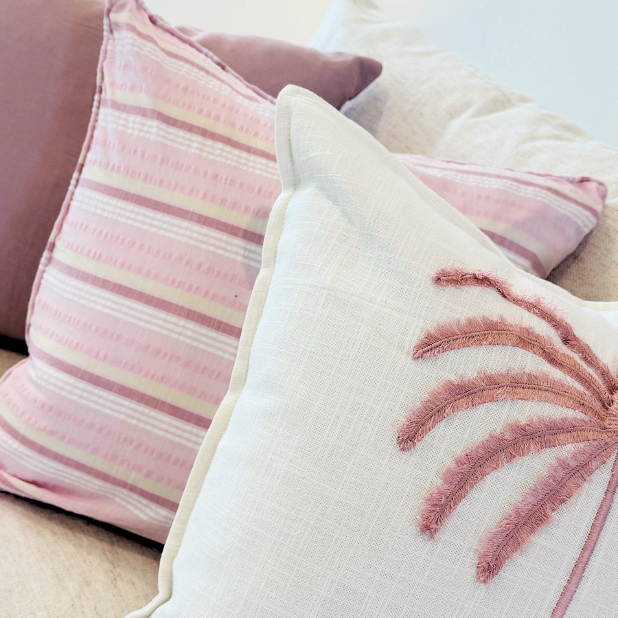 Decorative cushion with pink palm leaf design on a neutral background.