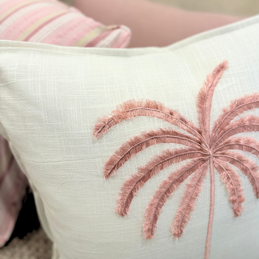 Decorative cushion with pink palm tree design on a neutral background.