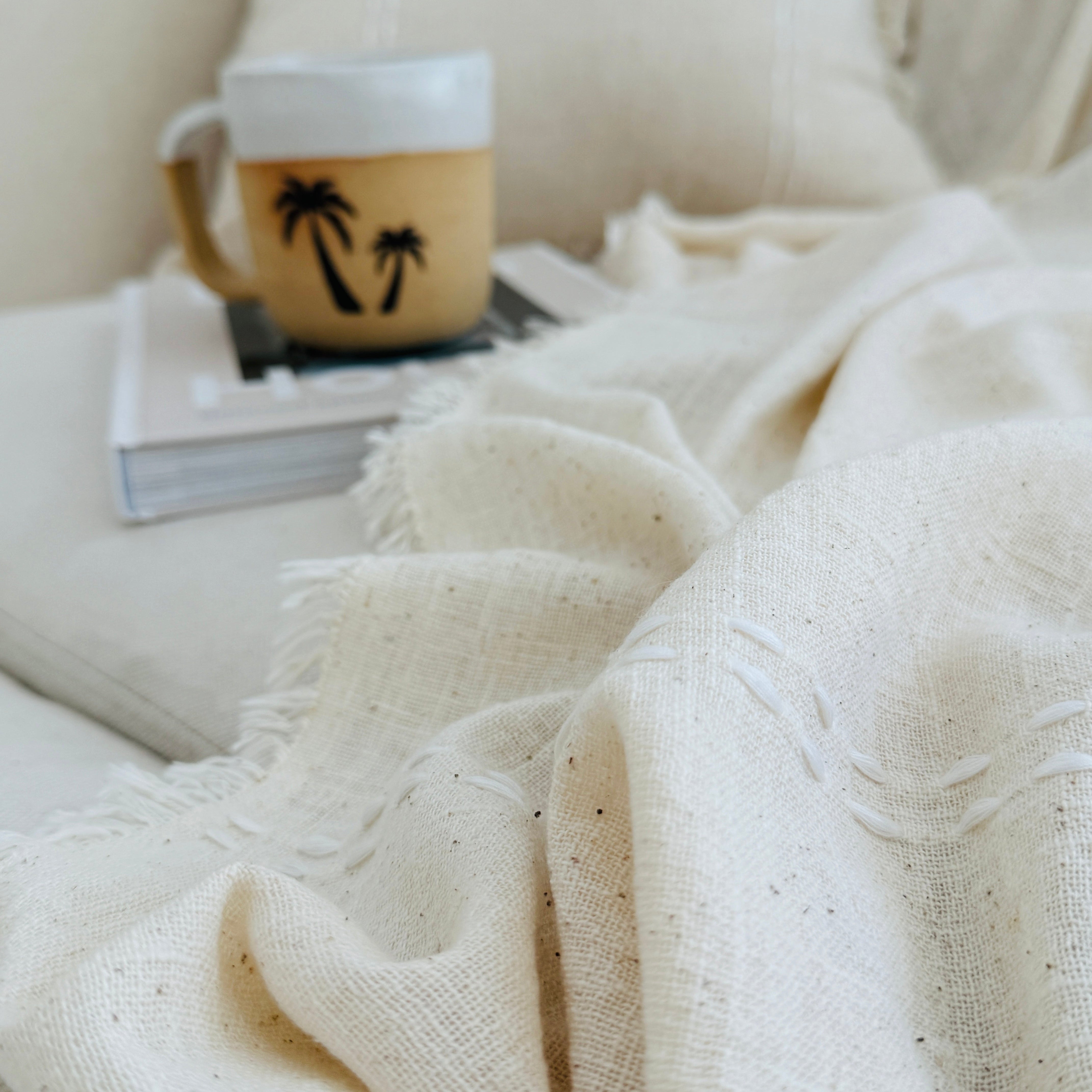 Cozy indoor setting with a blanket, mug, and book on a couch.