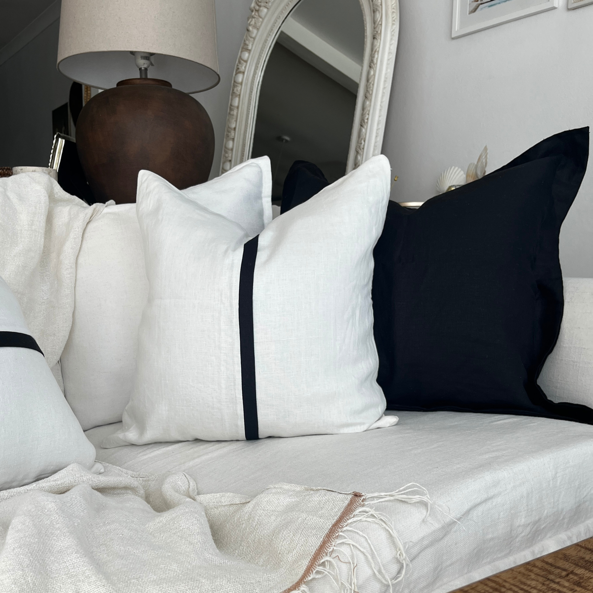 Ivory and black square linen throw cushion set styled on a white couch with a fringed throw blanket.