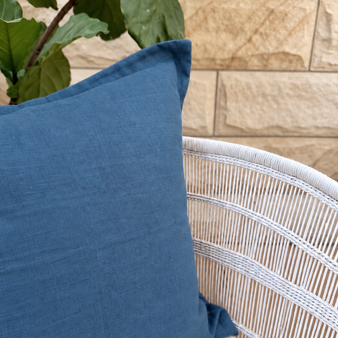 Blue linen cushion close-up styled on a white woven chair.