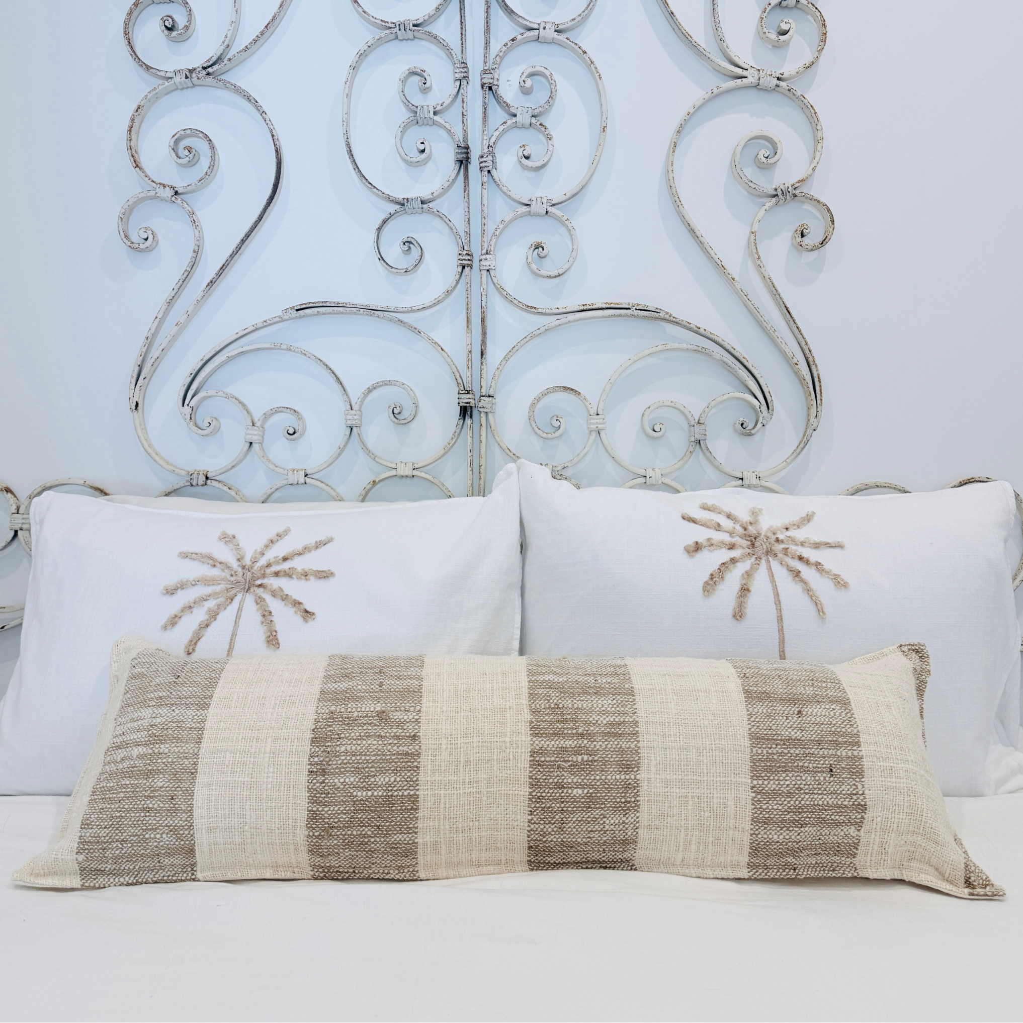 Decorative cushion with intricate patterns on a bed with an ornate metal headboard.