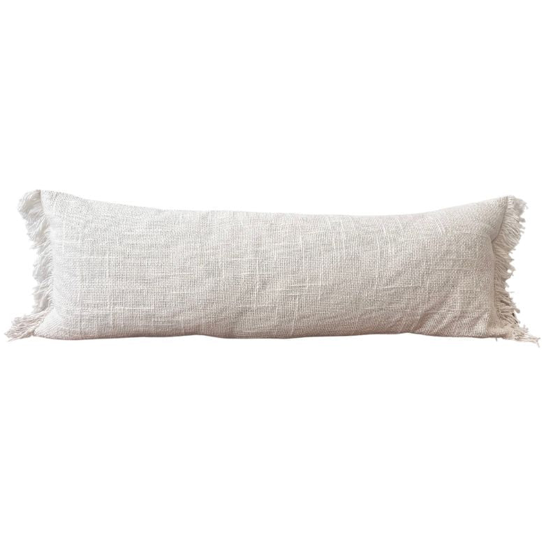 A cream-colored, fringed cushion cover with a textured weave pattern.
