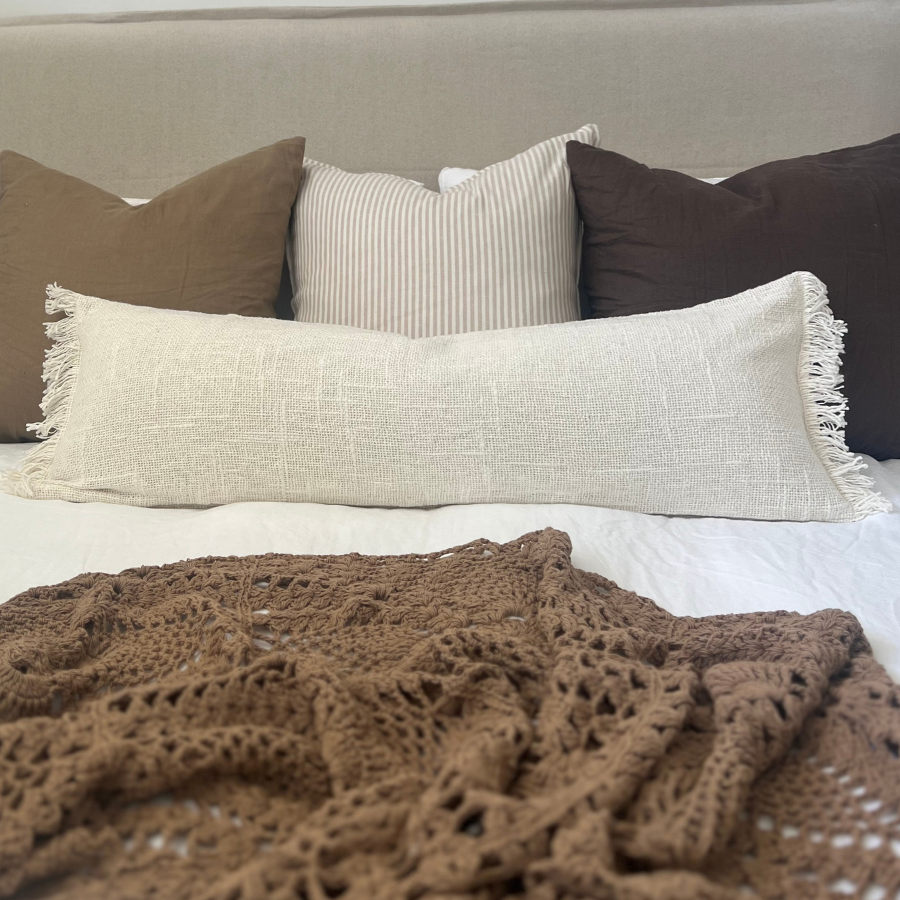White and brown cushions on a bed with blanket.