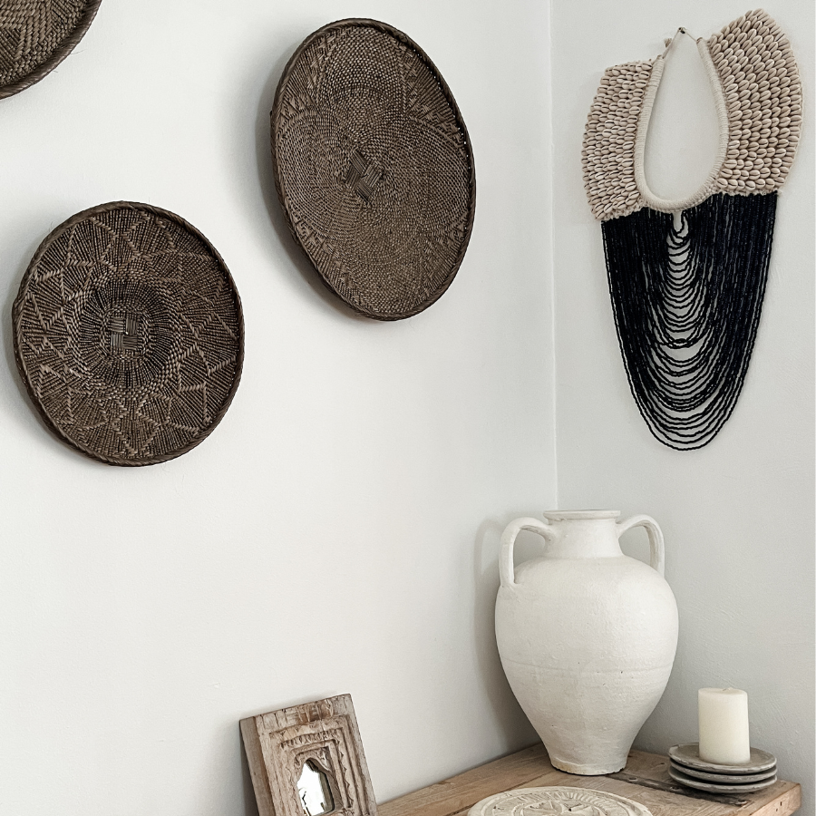 Black beaded decor hanging on wall with woven decor and vase.