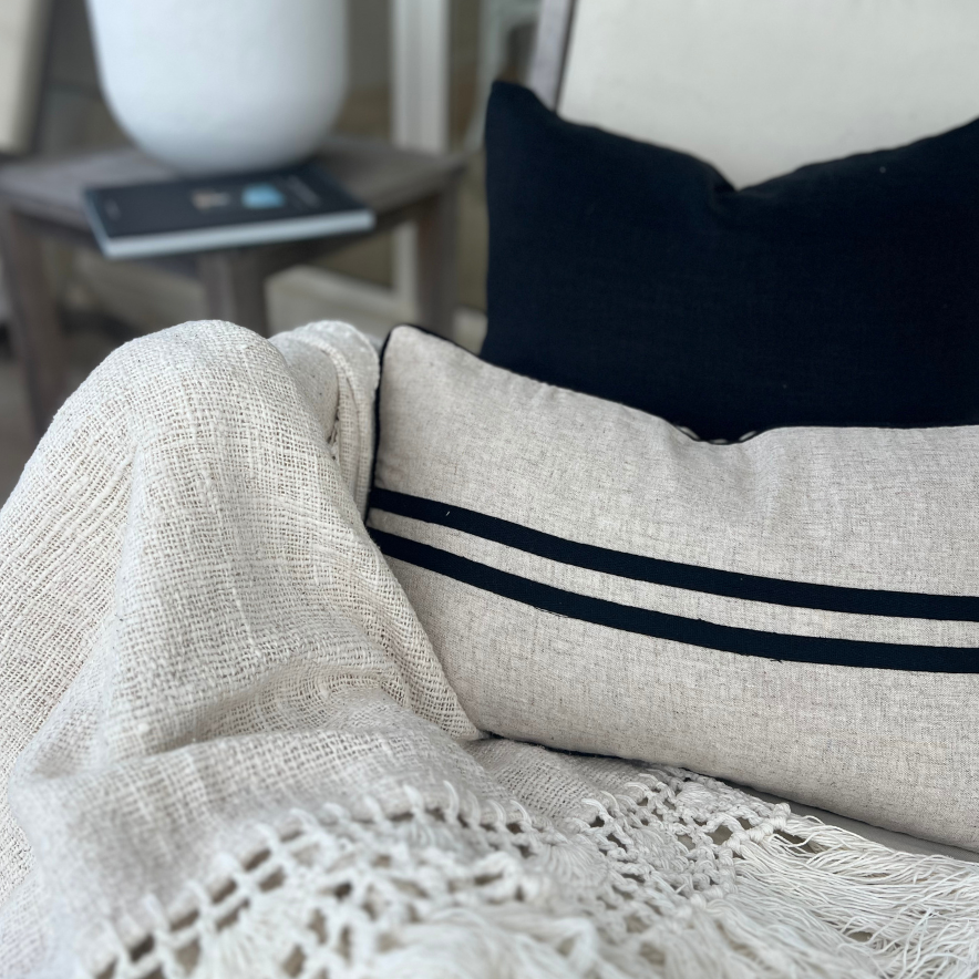 Striped cushion and solid black cushion on a chair with blanket.