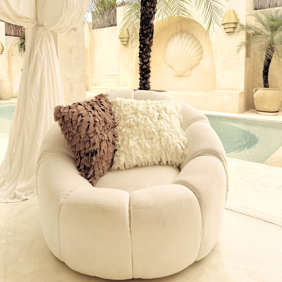 White chair with decorative cushion in a tropical outdoor setting with palm trees and a pool.