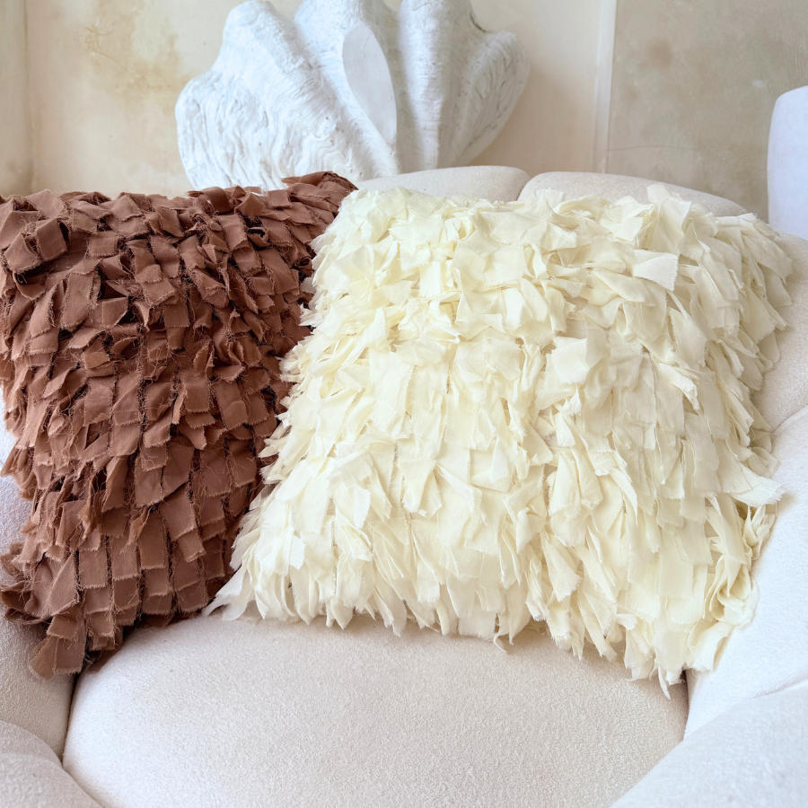 Two textured cushion, one brown and one white, on a beige sofa.