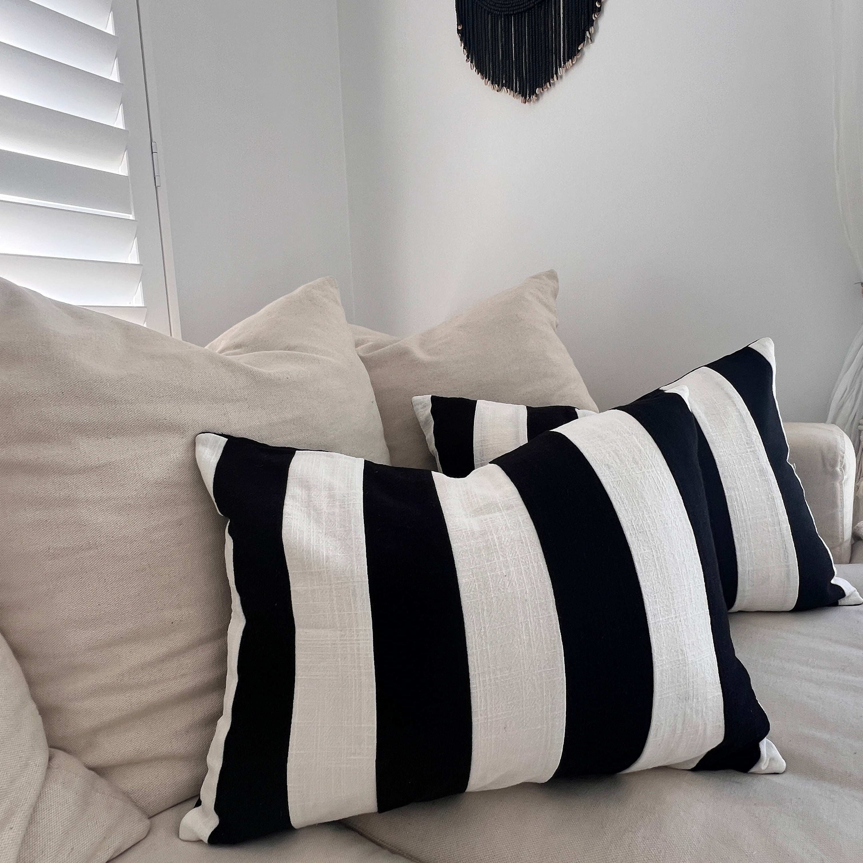 Two black and white striped cushion covers on a sofa with a black timber-beaded wall hanging above them.