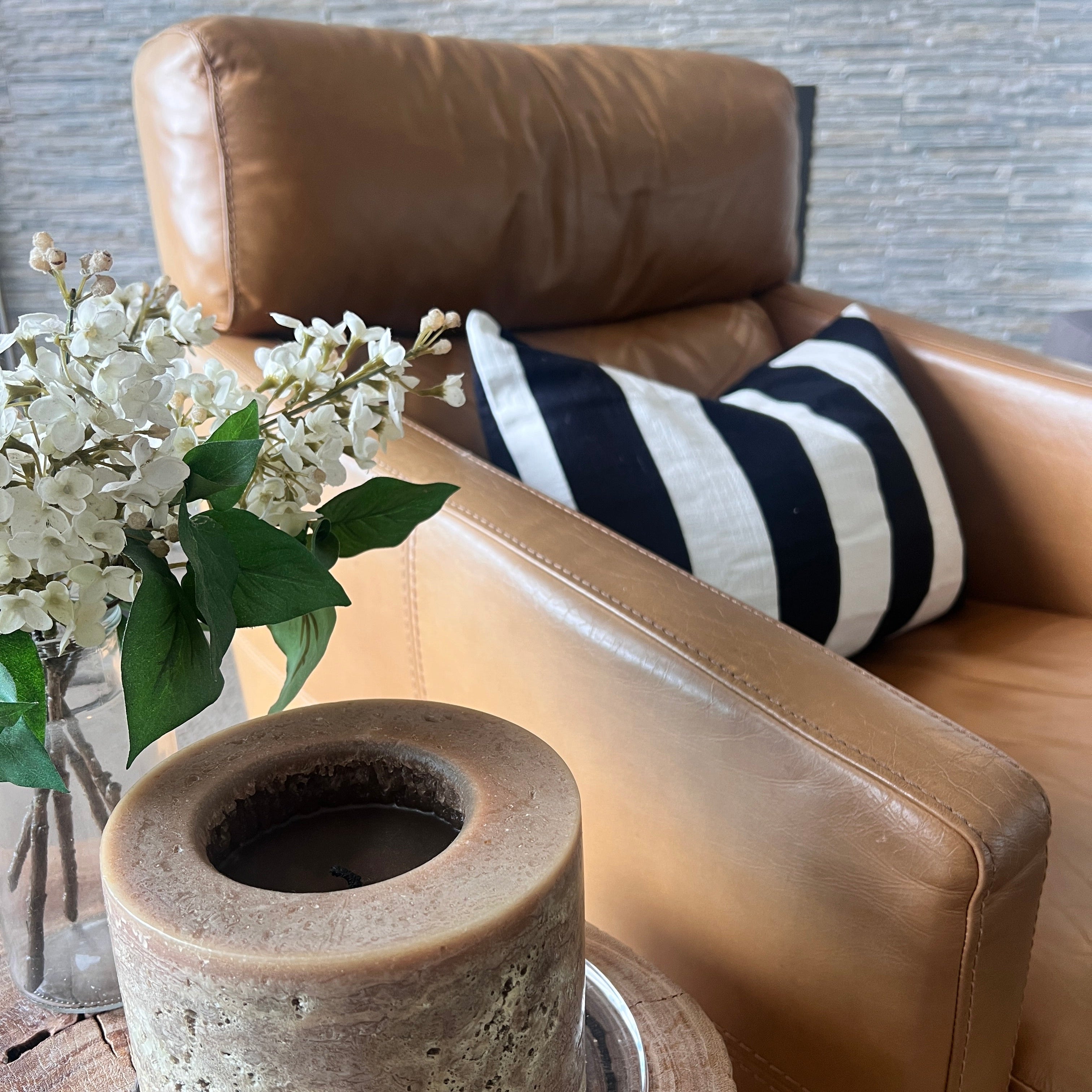 Brown leather armchair with a striped cushion and a vase of flowers on a wooden table.