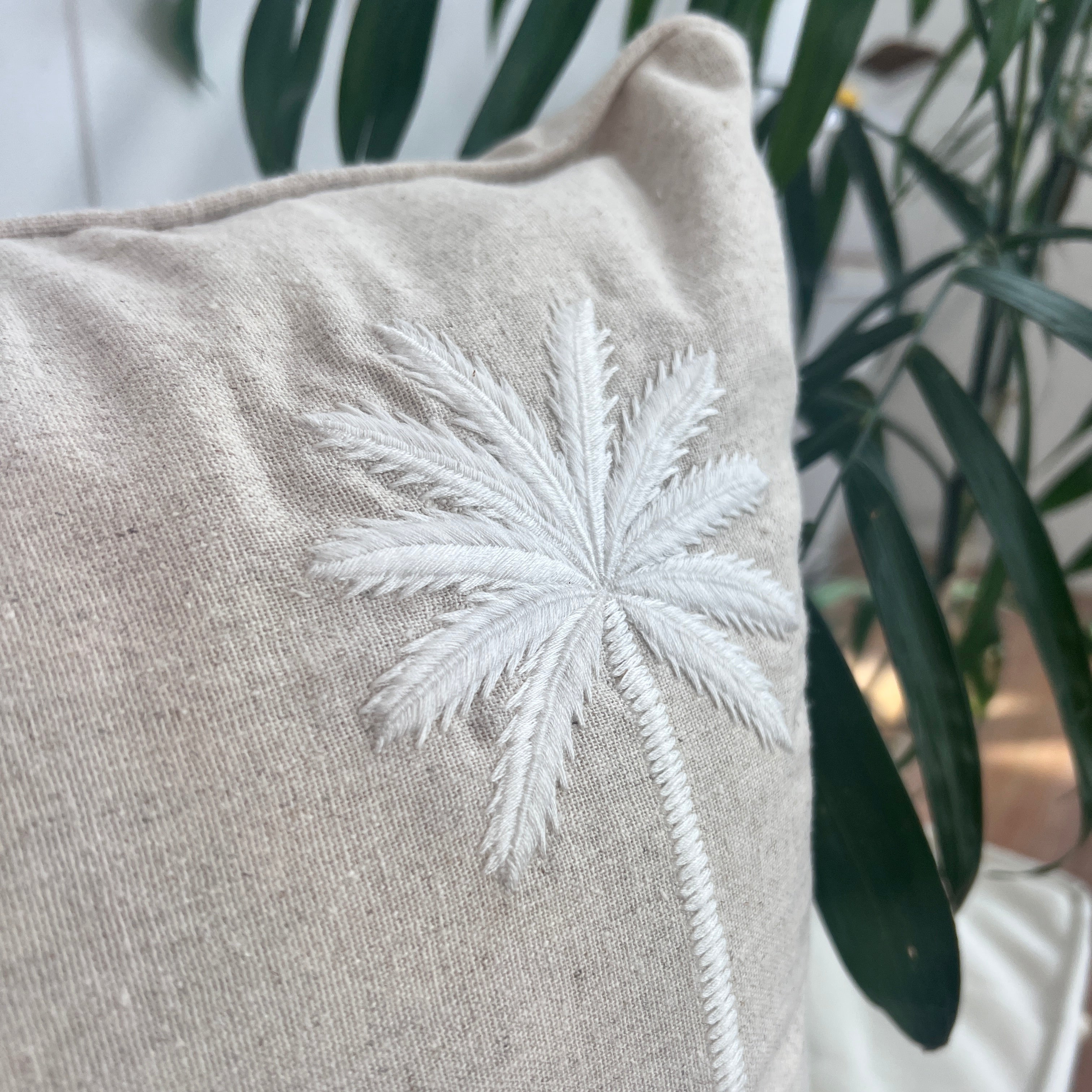 Beige cushion with white embroidered star design against a blurred plant background.