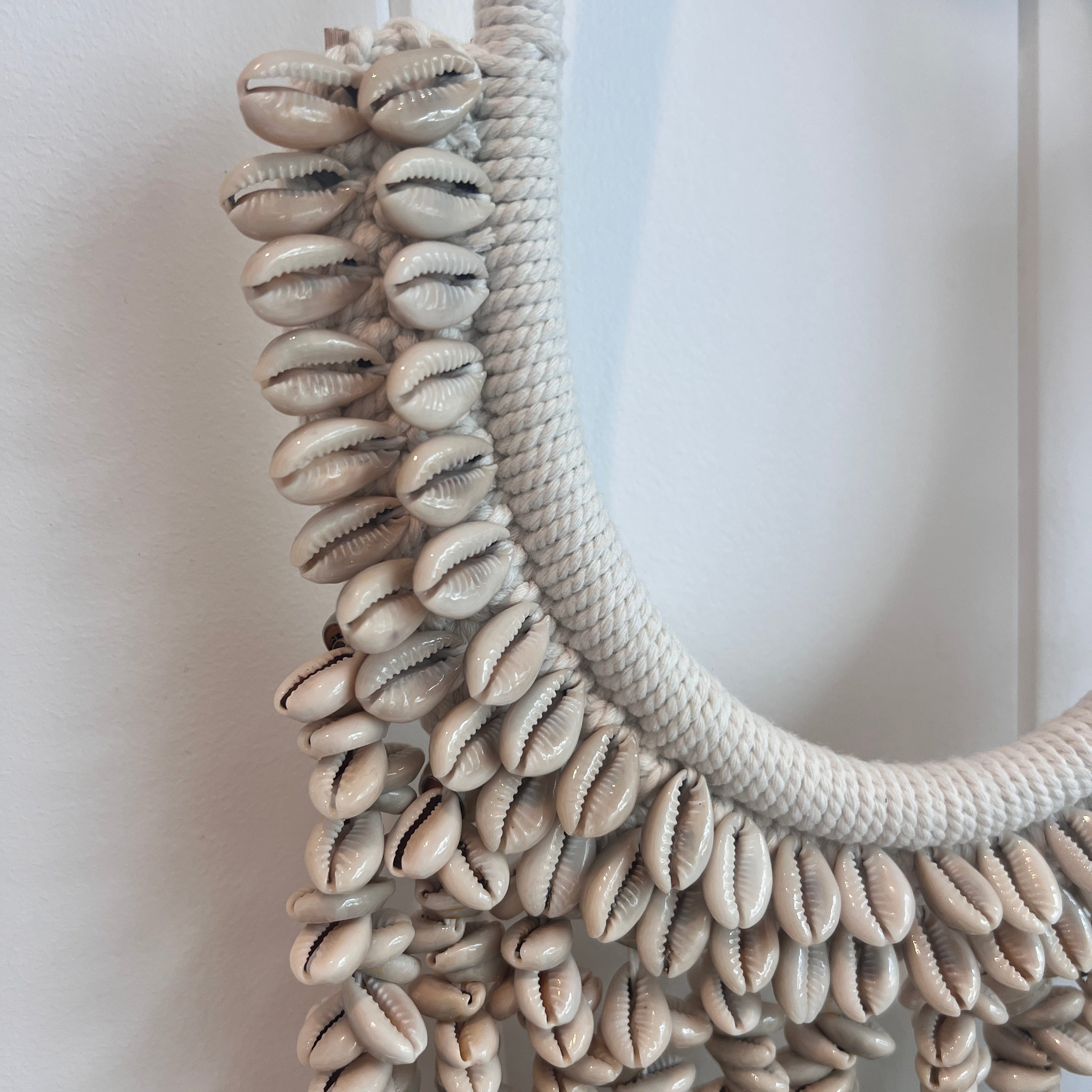 Decorative wreath made of cowrie shells on a white background.