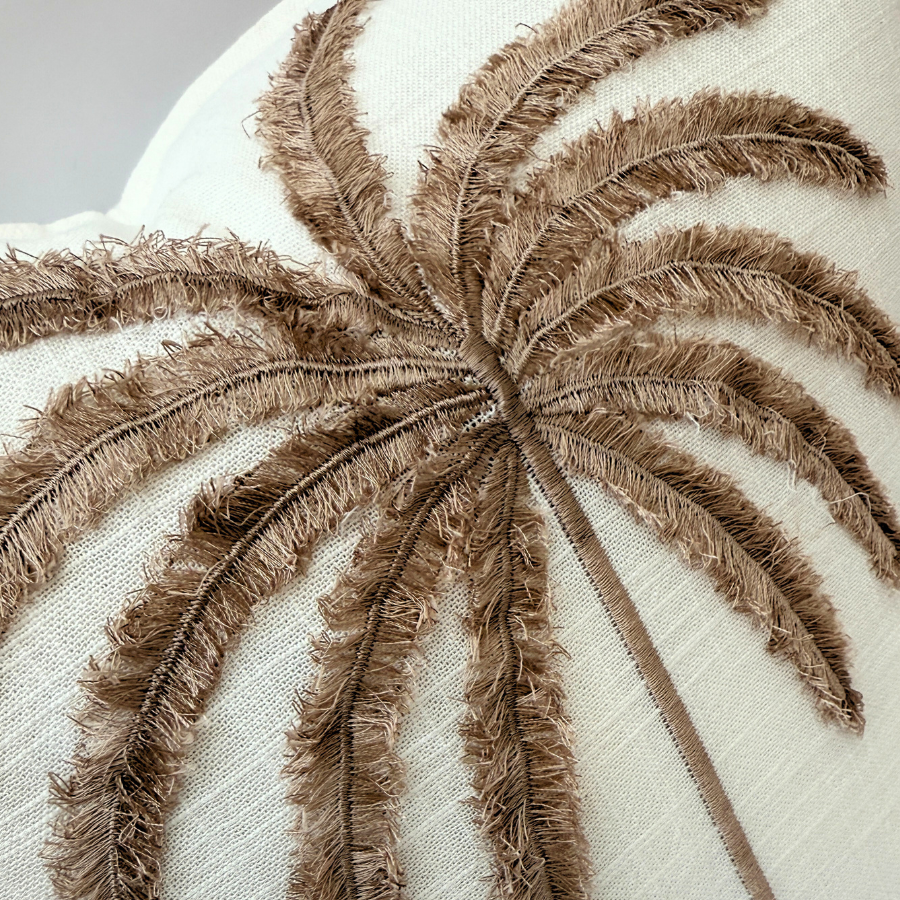 Close-up of a brown embroidered palm leaf design on a beige fabric background