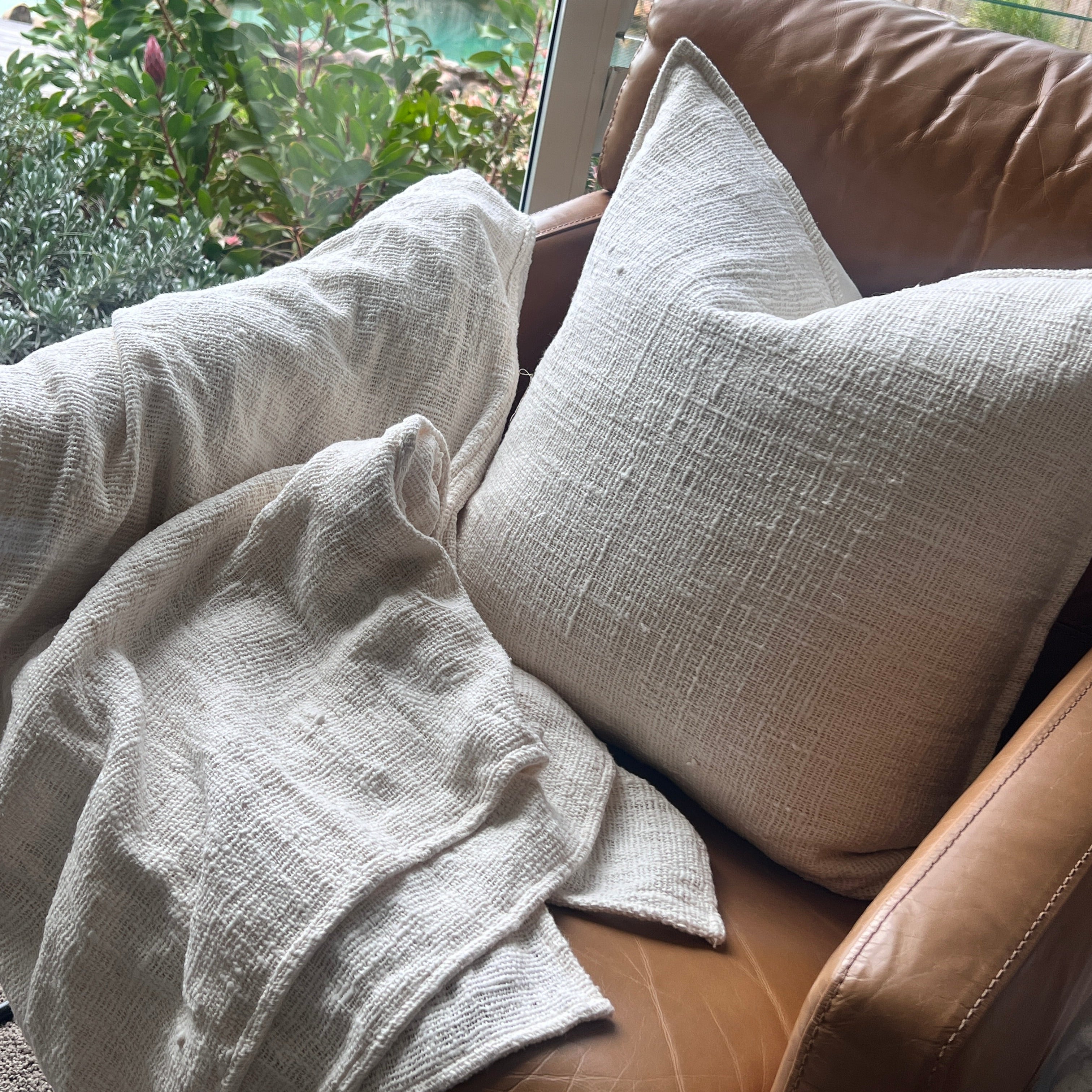 Textured cushion on a sofa with a window view of greenery.
