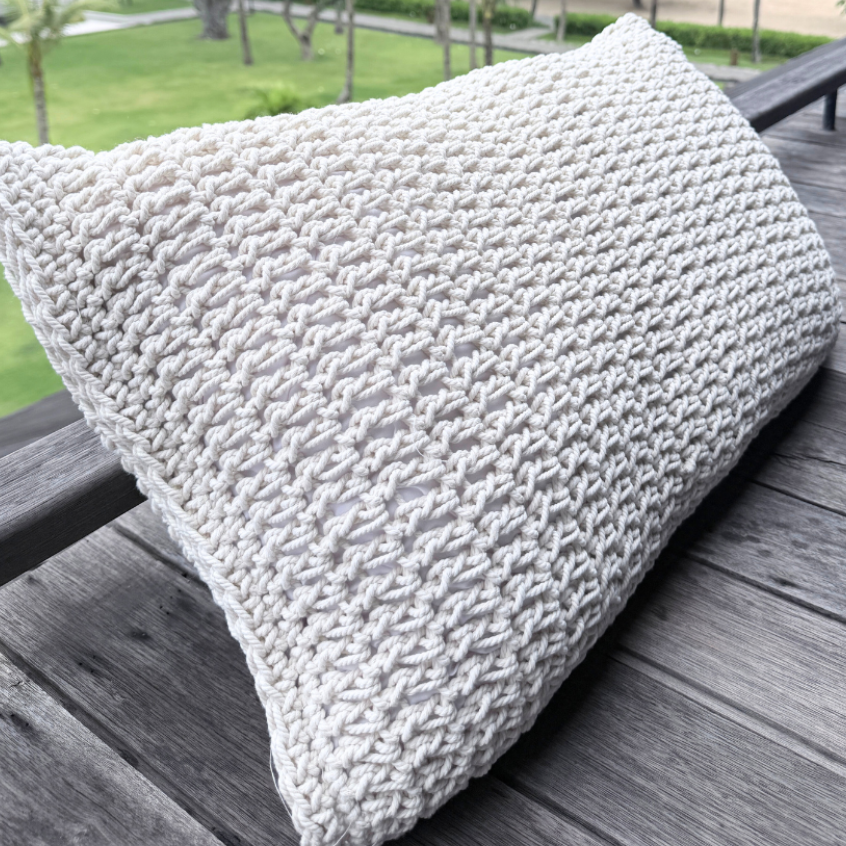 Textured white cushion on a wooden deck with a scenic background of trees and water.