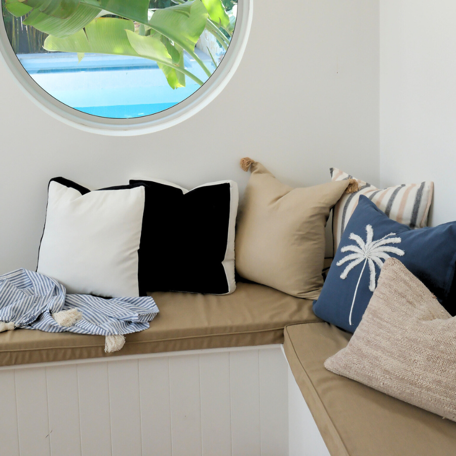 Circular window with a view of greenery and a pool, featuring a cushioned bench with cushions.
