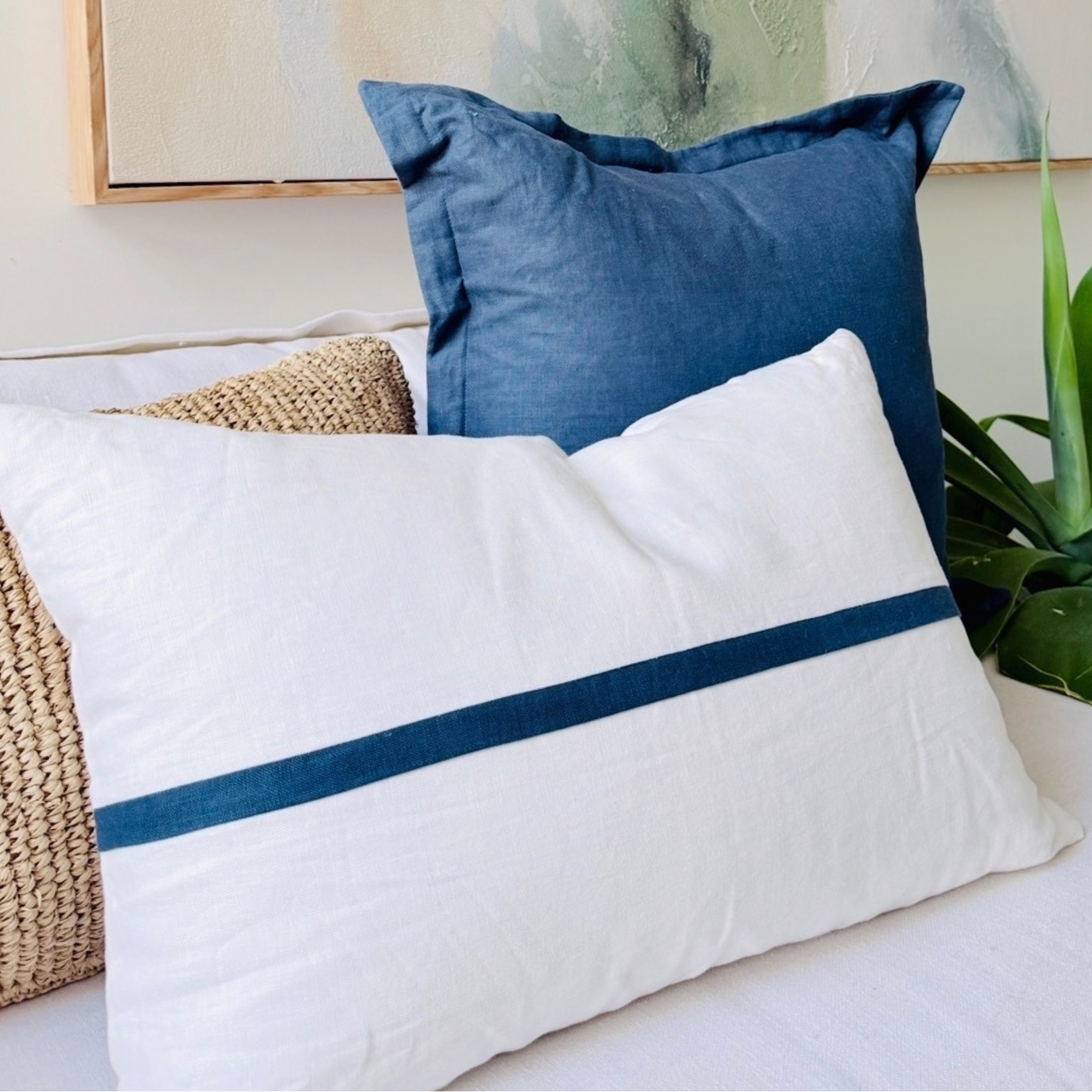 Decorative cushion with blue and white stripes on a couch, with a plant and abstract painting.