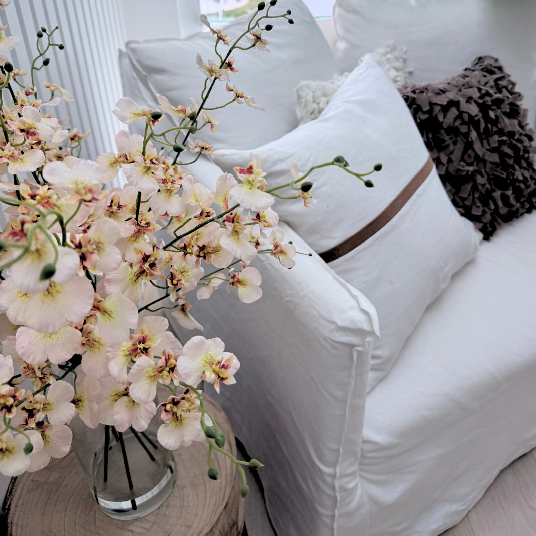 White sofa with decorative cushion and a vase of flowers on a wooden table.