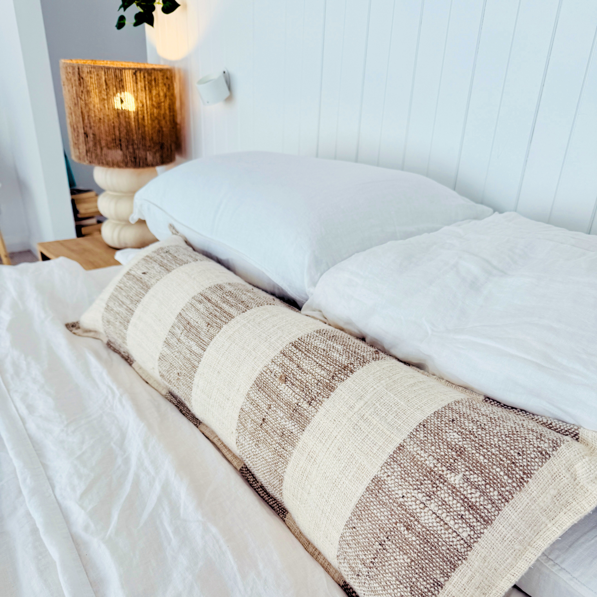 Neatly made bed with striped throw blanket and white cushion in a bedroom setting.