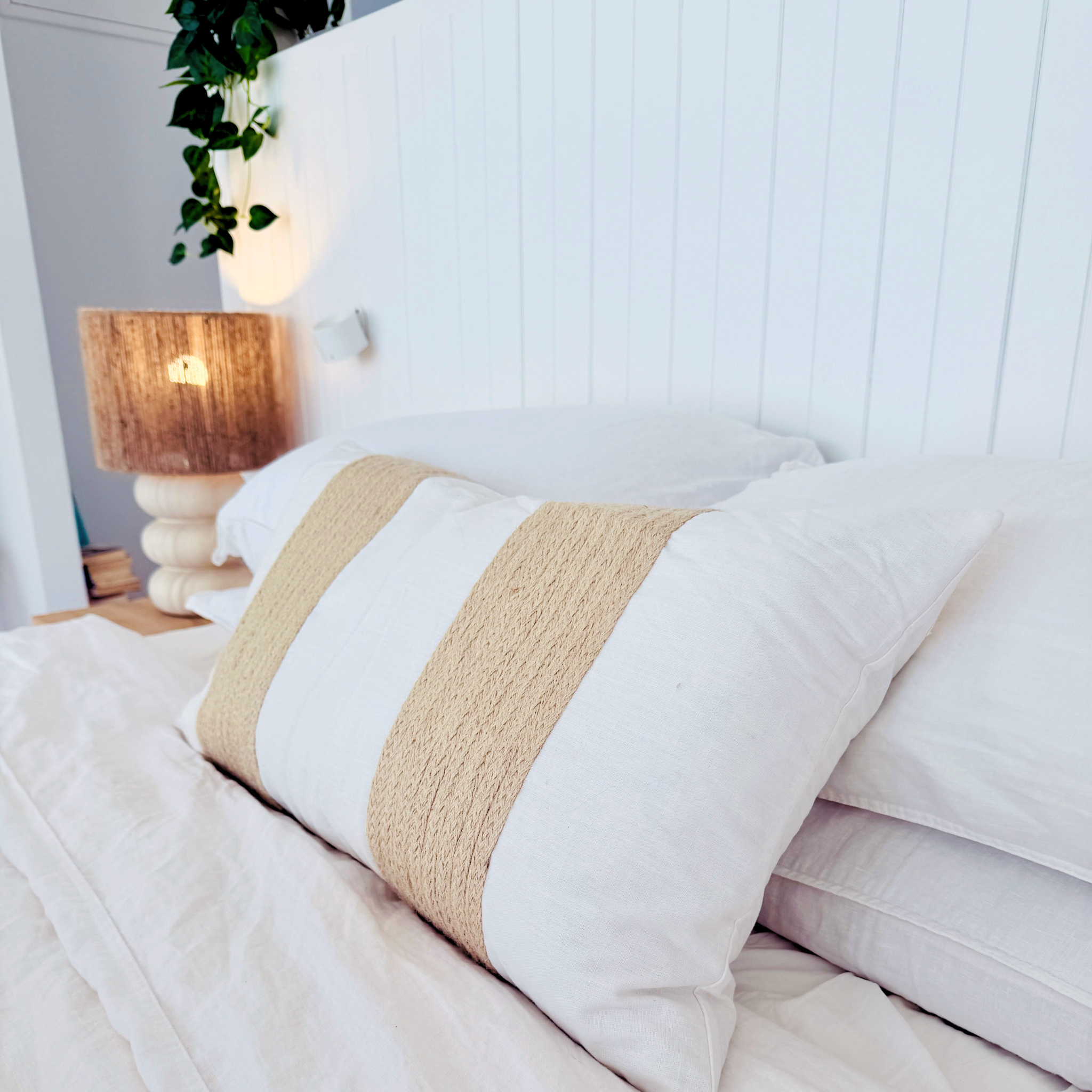 White bed with beige striped cushion and wooden nightstand in a bright room.