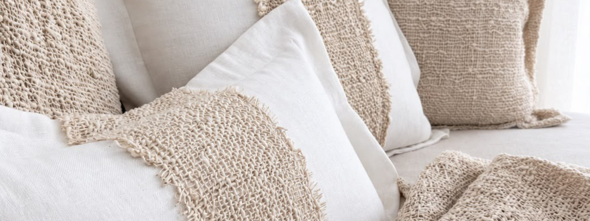 A close-up of neutral-toned pillows with textured woven bands and a matching beige throw blanket on a sofa.