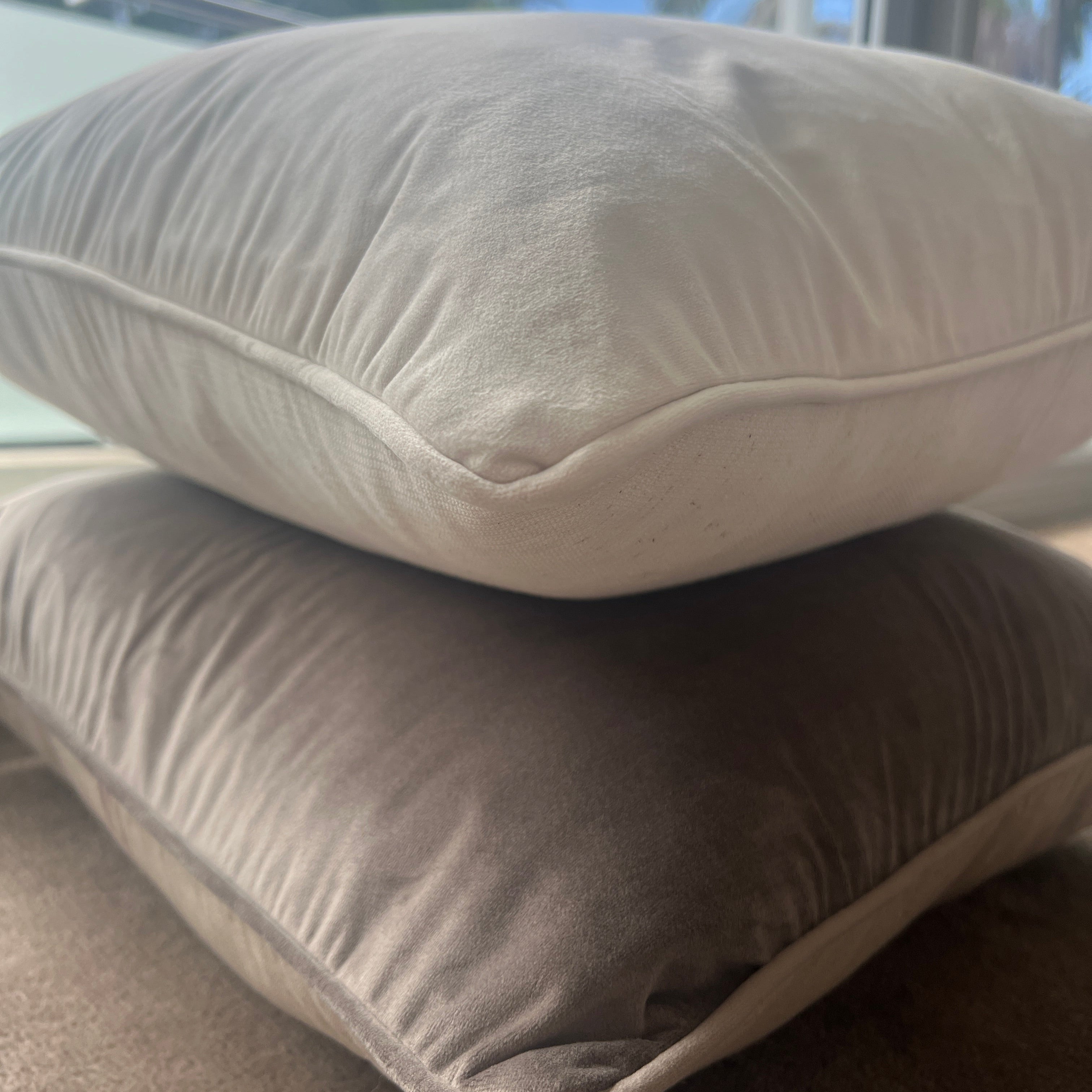 Two velvet cushions stacked on top of each other, with the top cushion in vanilla color and the bottom one in mocha color.