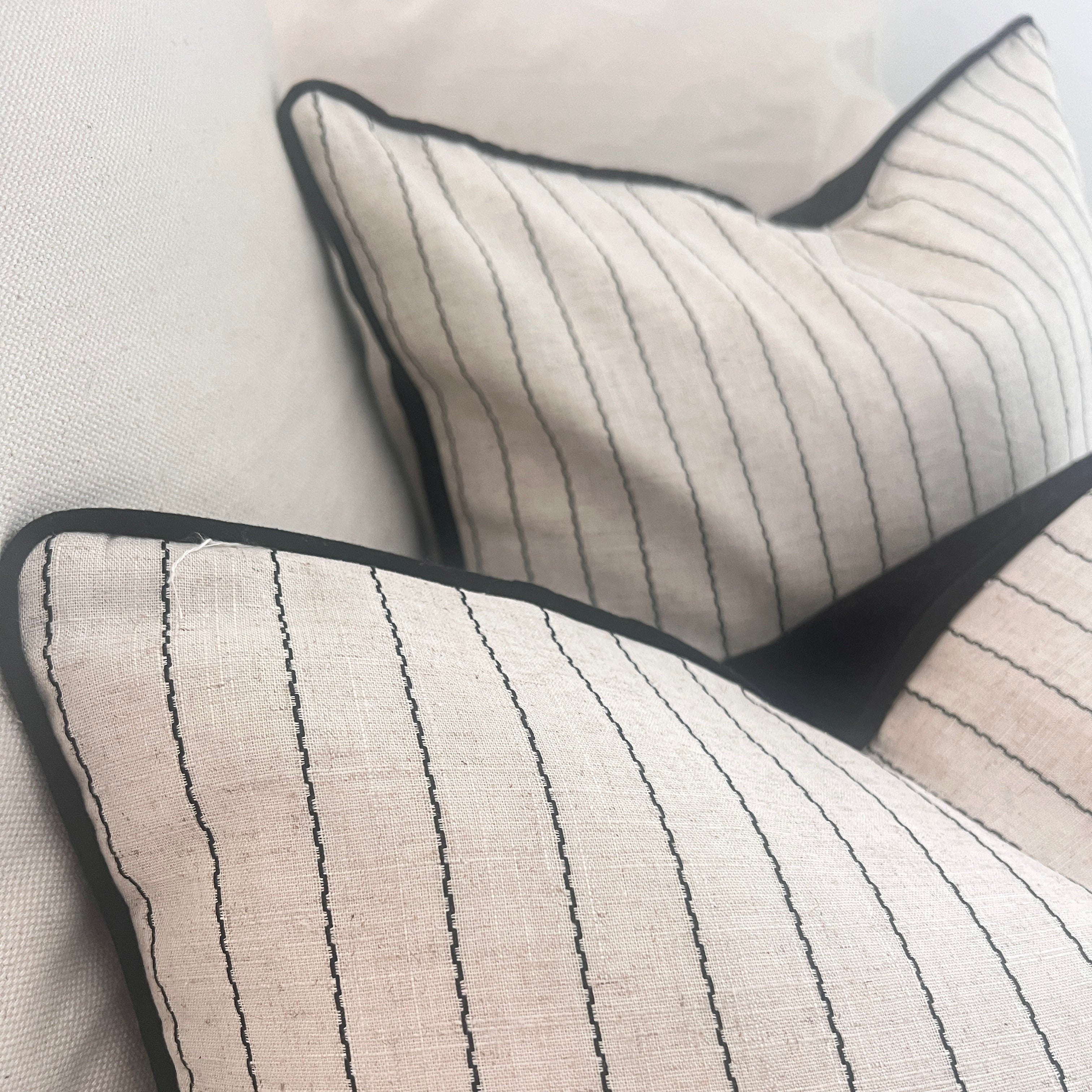 Two square throw cushion with a fine cotton stripe pattern in black stitching, one smaller than the other, partially overlapping.