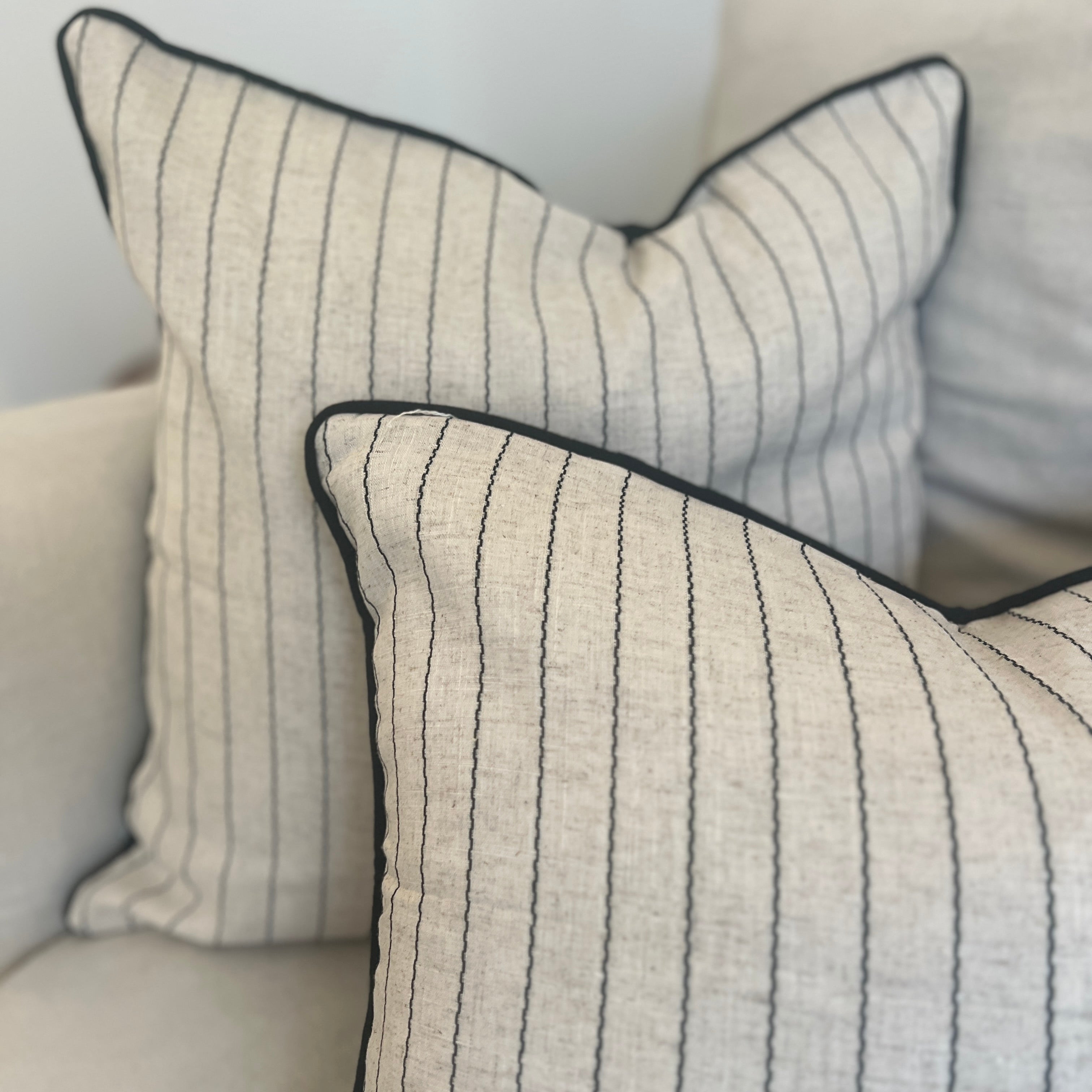 Two rectangular cushions with a fine stripe design in natural color with black stitching, and a black piped edge on the back.