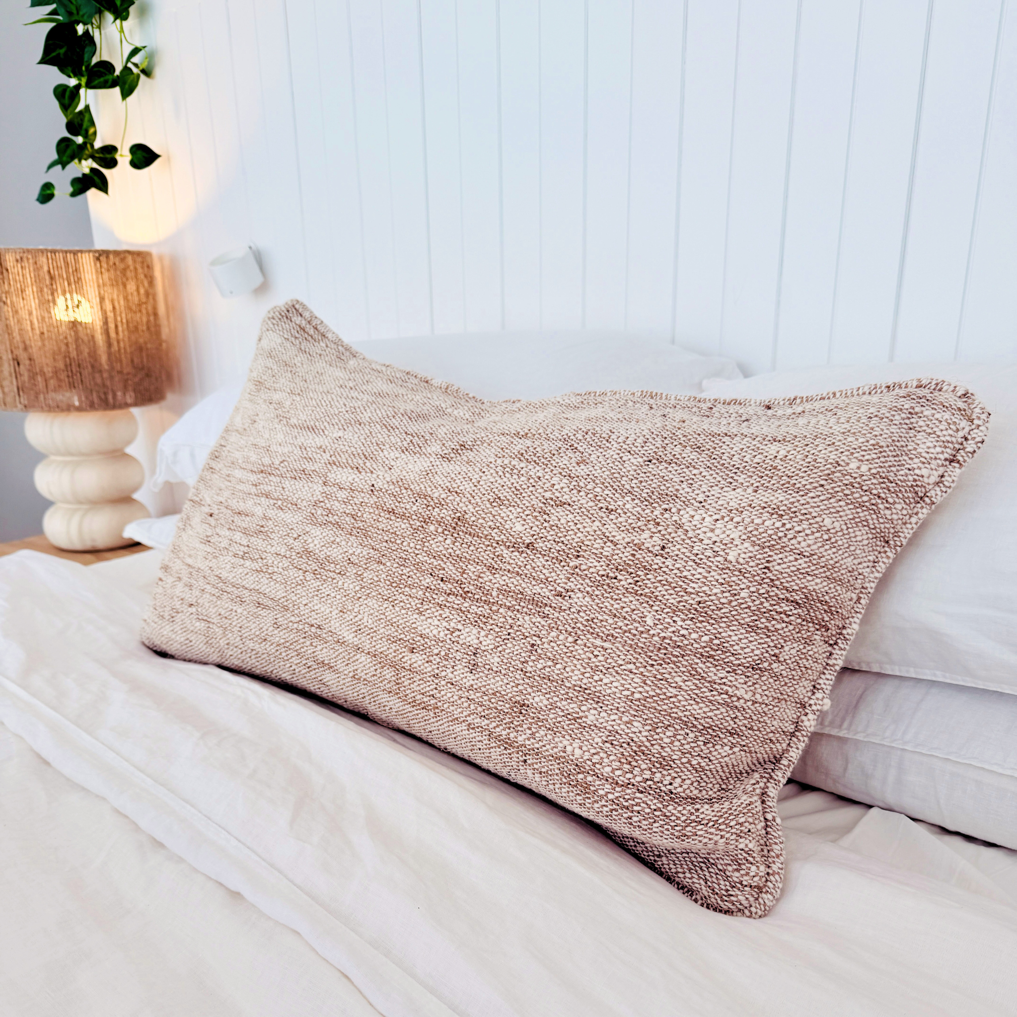 Textured pink cushion on a bed with a lamp and plant in the background.