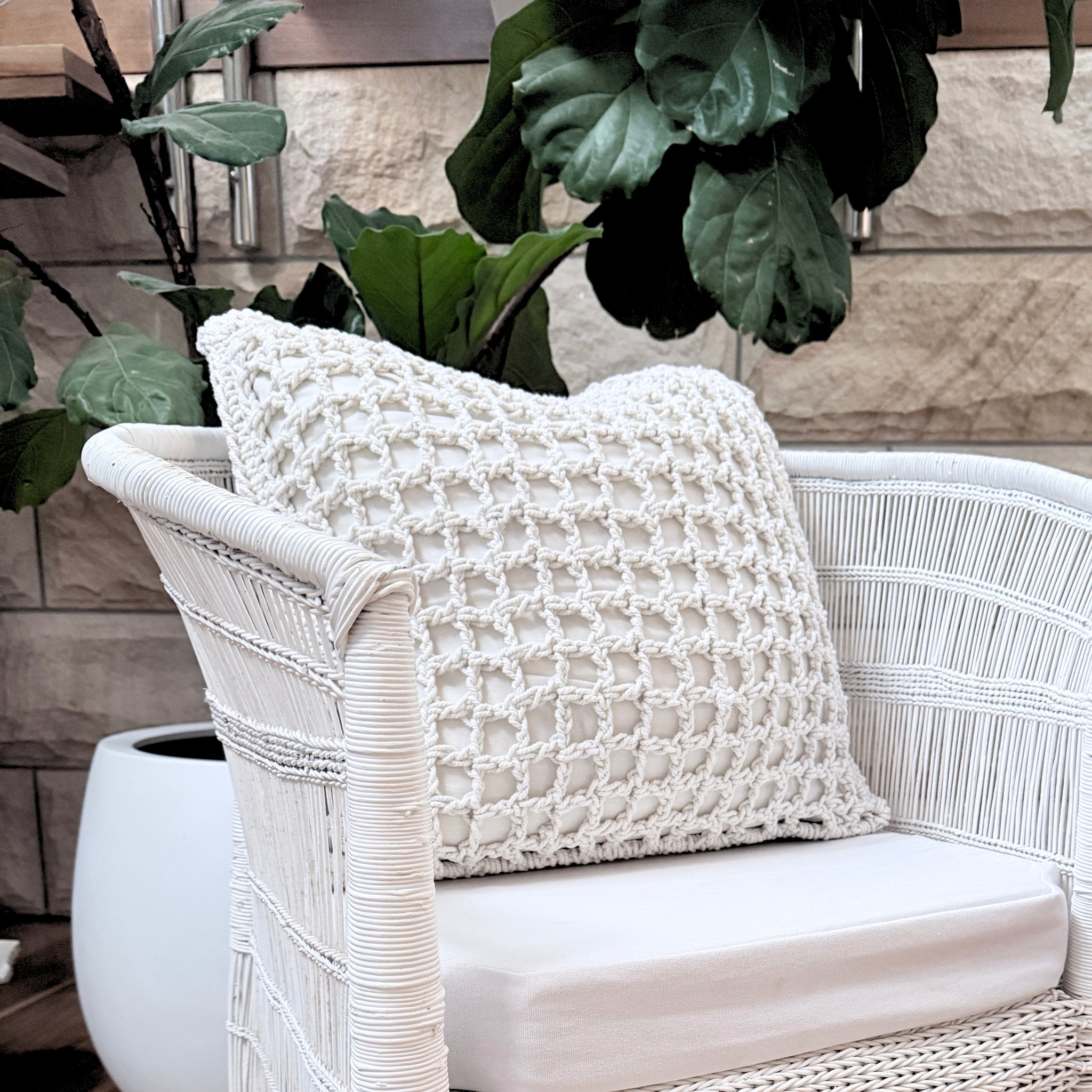 White wicker chair with a textured white cushion against a wooden wall with plants.