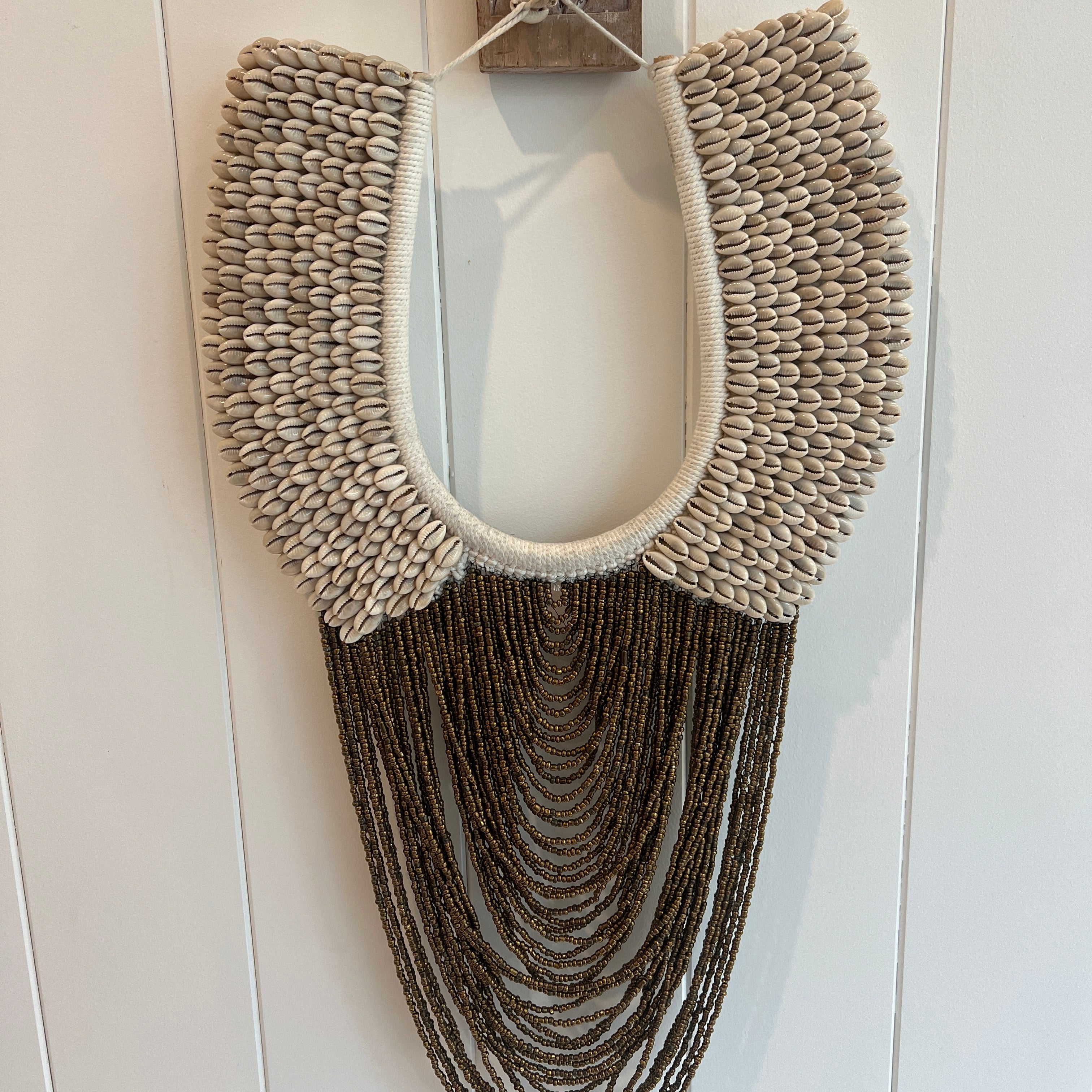 A wall-mounted cowrie shell necklace with bronze beading and a cotton macrame backing.